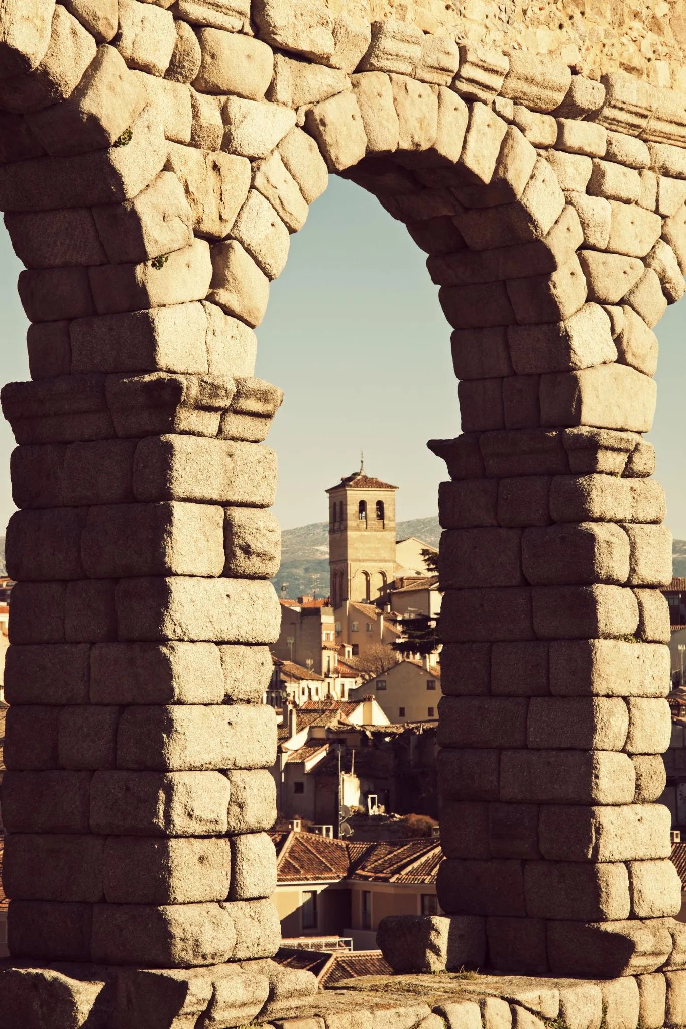 Arco de piedra romano con vista a ciudad española y torre, inspiración para ropa con legado histórico